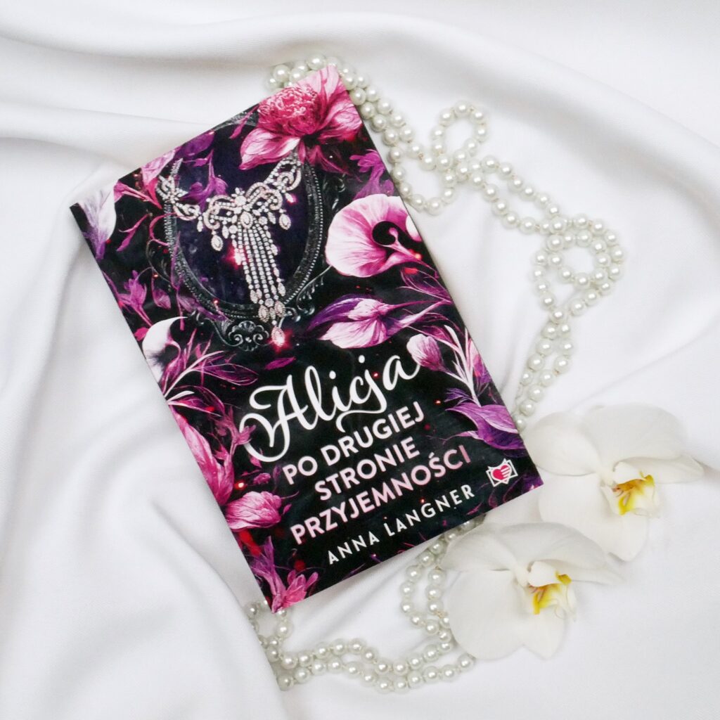 Okładka książki „Alicja. Po drugiej stronie przyjemności” – Anna Langner Okładka książki „Alicja. Po drugiej stronie przyjemności” autorstwa Anny Langner na białej tkaninie z perłami i orchideami