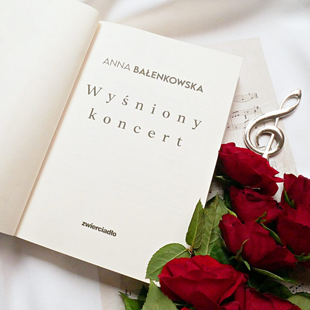 Anna Balenkowska „Wyśniony koncert” Strona tytułowa książki „Wyśniony koncert” Anny Bałenkowskiej, na tle nut, czerwonych róż i srebrnego klucza wiolinowego.
