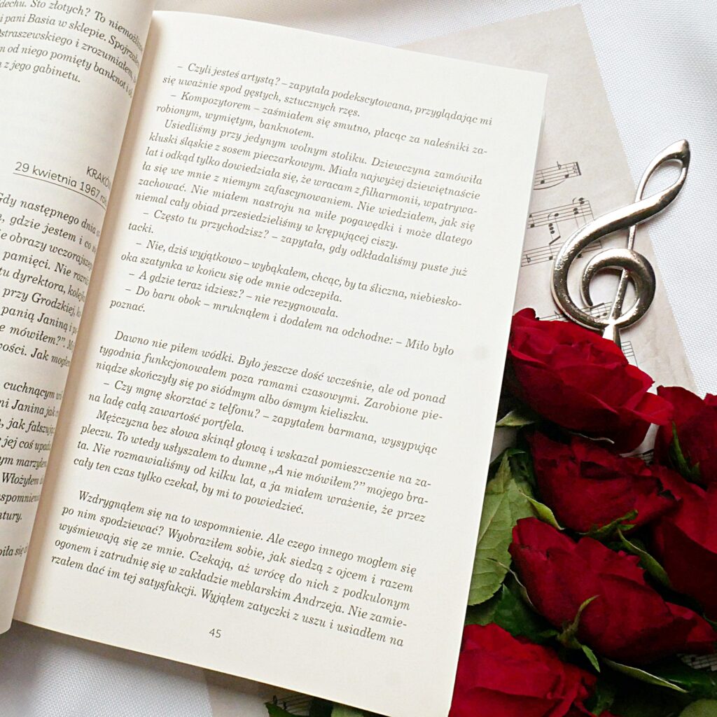 Fragment książki Anny Balenkowskiej „Wyśniony koncert” Otwarta książka „Wyśniony koncert” na stronie z tekstem fabularnym, obok czerwone róże, nuty i ozdobny klucz wiolinowy.