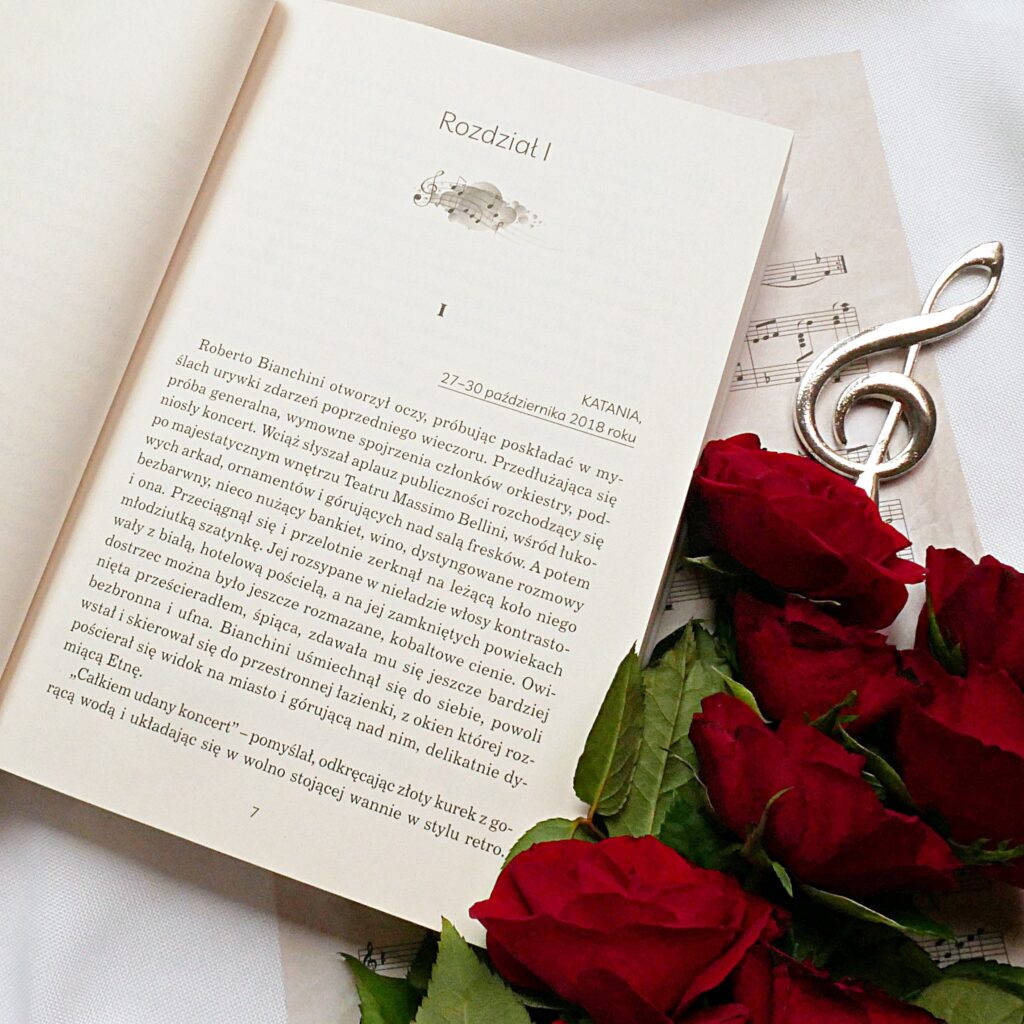 Recenzja książki Anny Balenkowskiej „Wyśniony koncert” Otwarta książka „Wyśniony koncert” na początku Rozdziału I, z tłem z nutami, różami i kluczem wiolinowym.