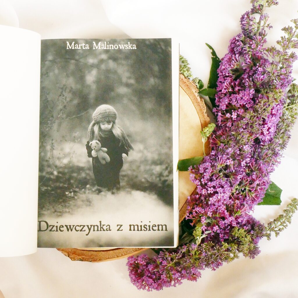 Strona tytułowa książki „Dziewczynka z misiem” Marty Malinowskiej Czarno-białe zdjęcie okładki książki „Dziewczynka z misiem” Marty Malinowskiej